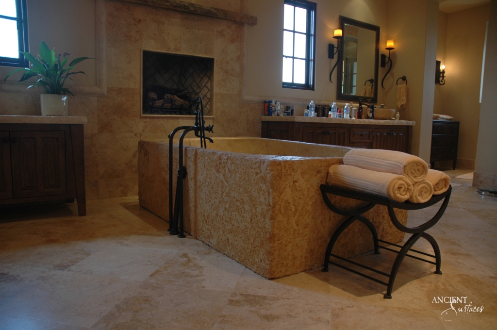 Centerpiece of a beautiful bathroom, a robust limestone bathtub by Ancient Surfaces, exuding warm tones and creating a cozy, inviting atmosphere while seamlessly blending with the architectural aesthetics of the space.
